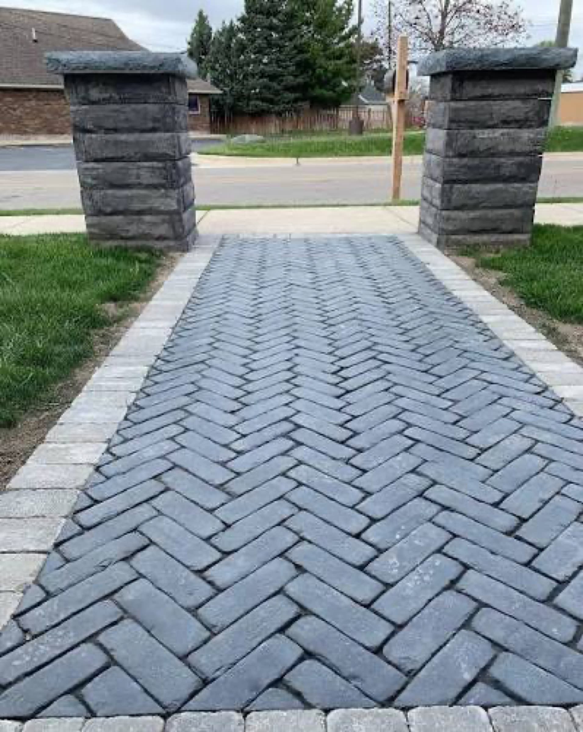 Charcoal herringbone paver walkway running between two stone pillars to the street
