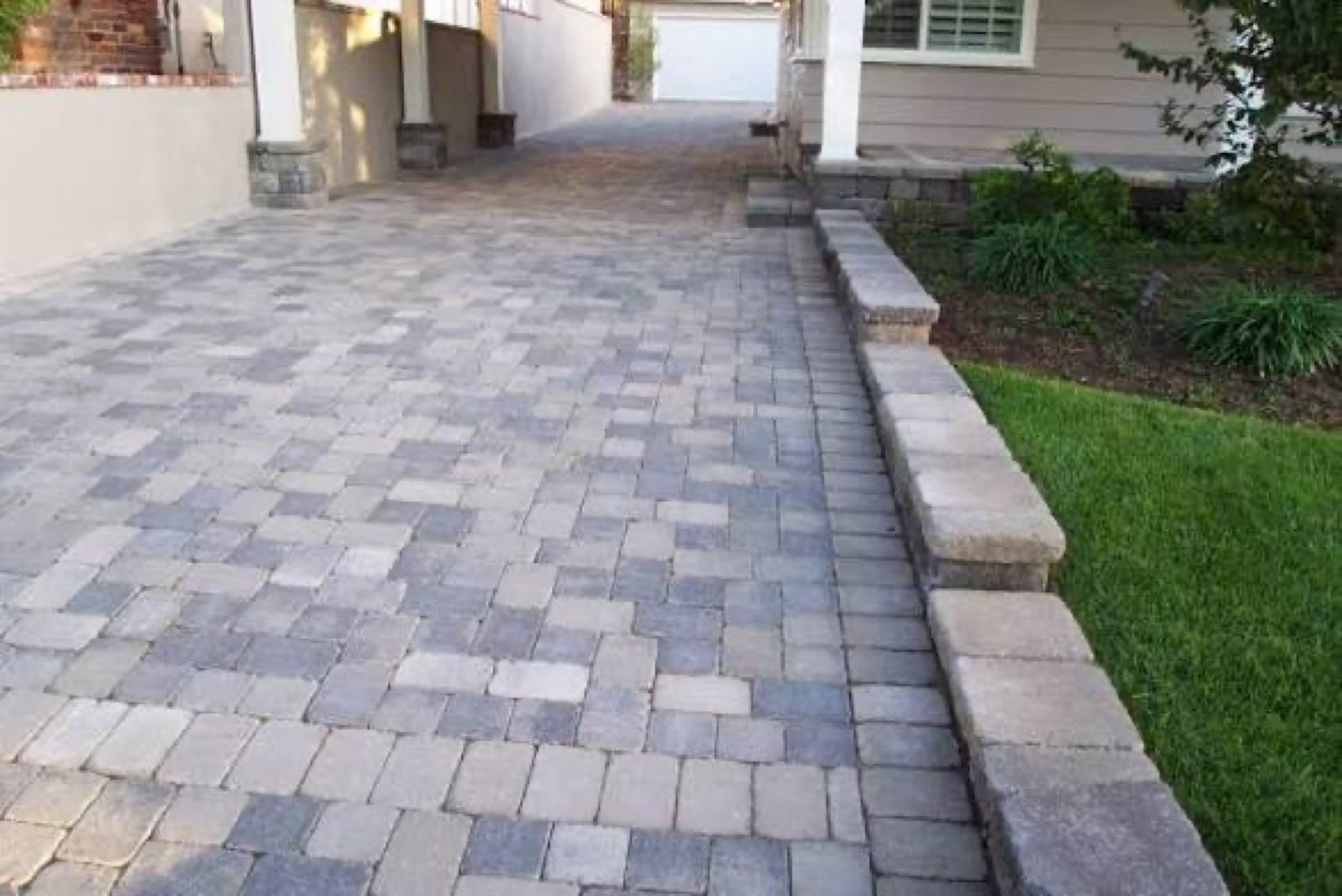Paver driveway in mixed greys with a matching block retaining wall along one edge