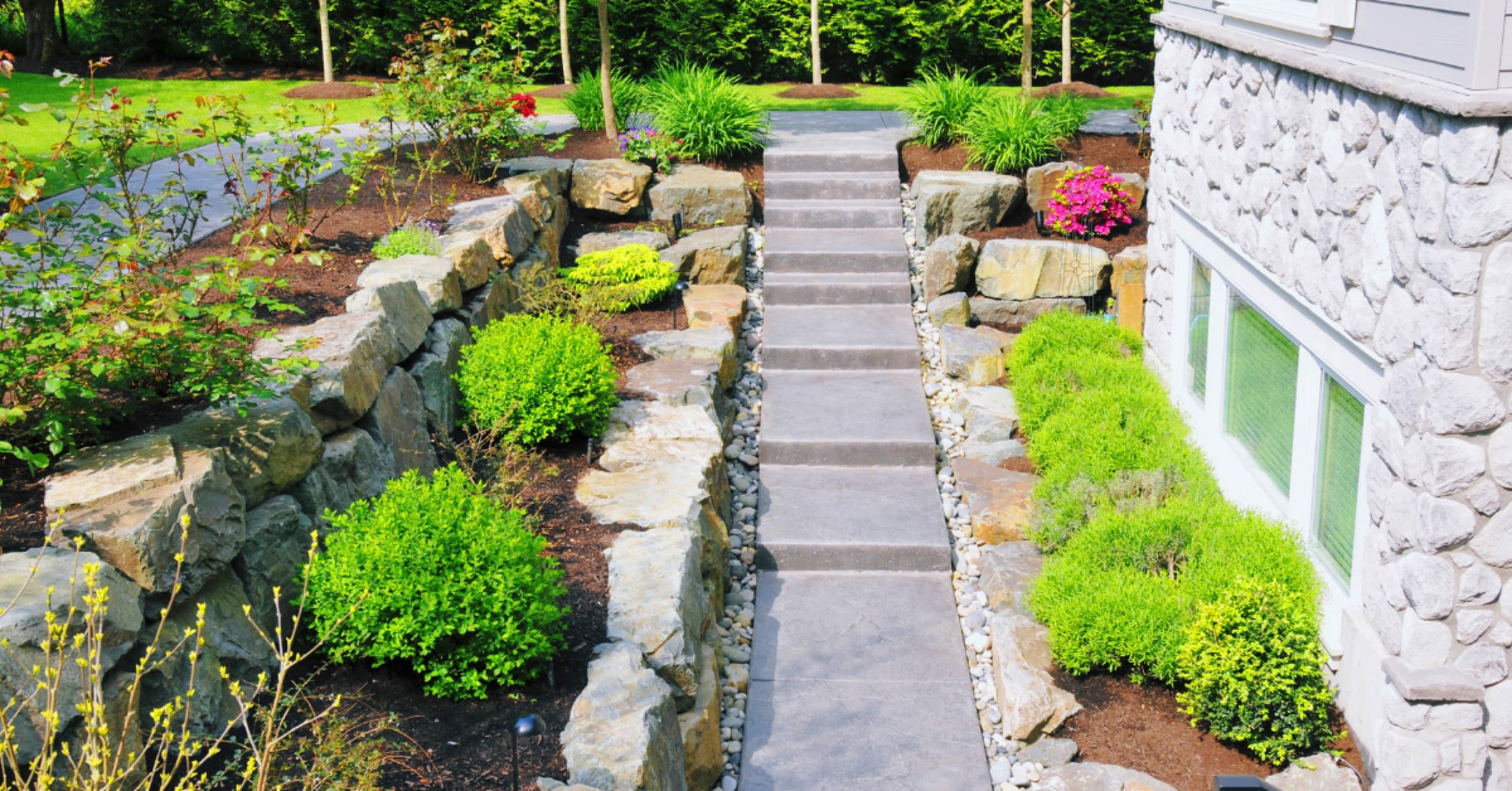 Terraced boulder retaining walls with a cut-stone stairway climbing between planted beds