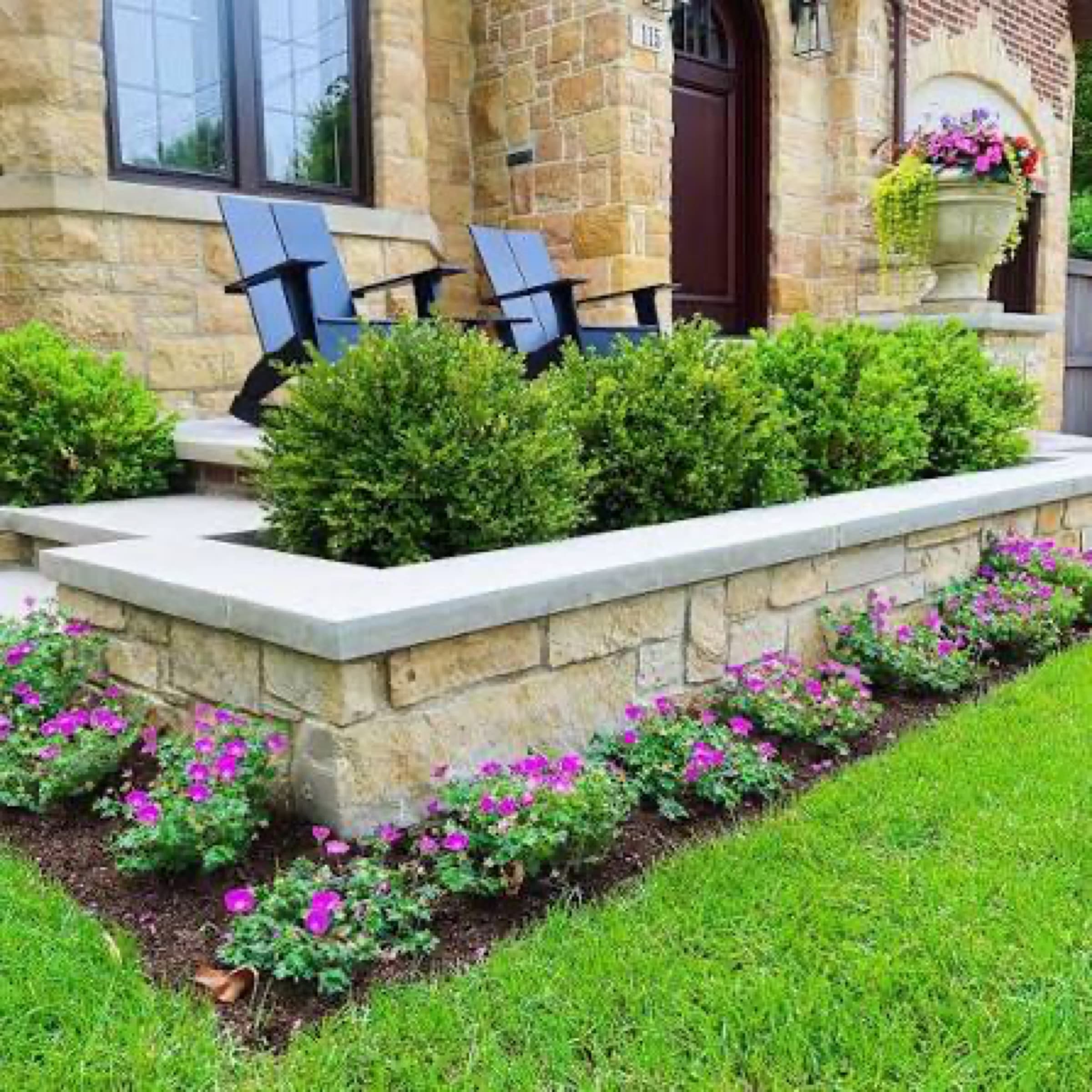 Cut-stone raised planter with a capstone edge, clipped boxwood above and flowering annuals at the base