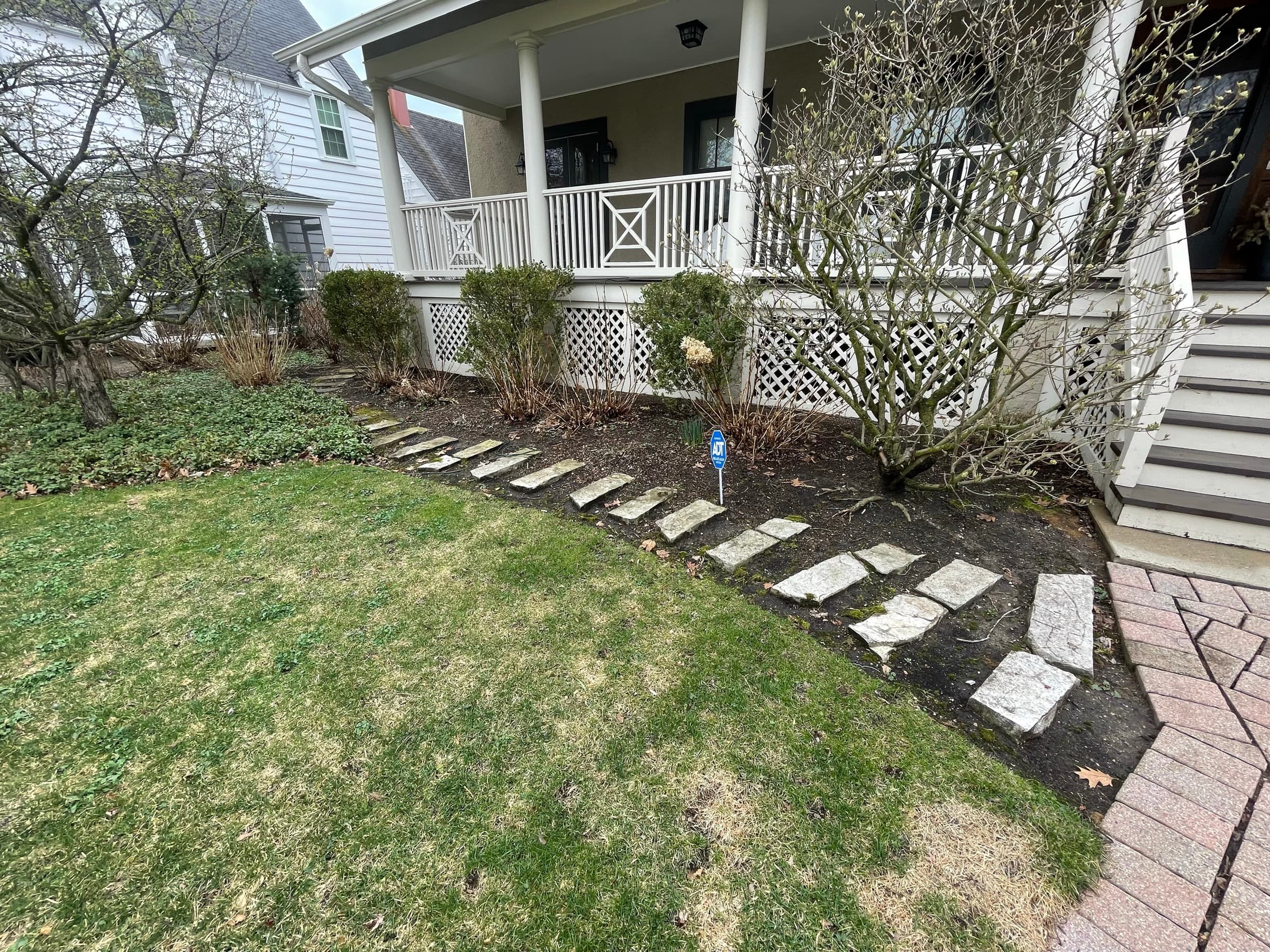 Irregular stone stepping stones being set into a bed along a front porch