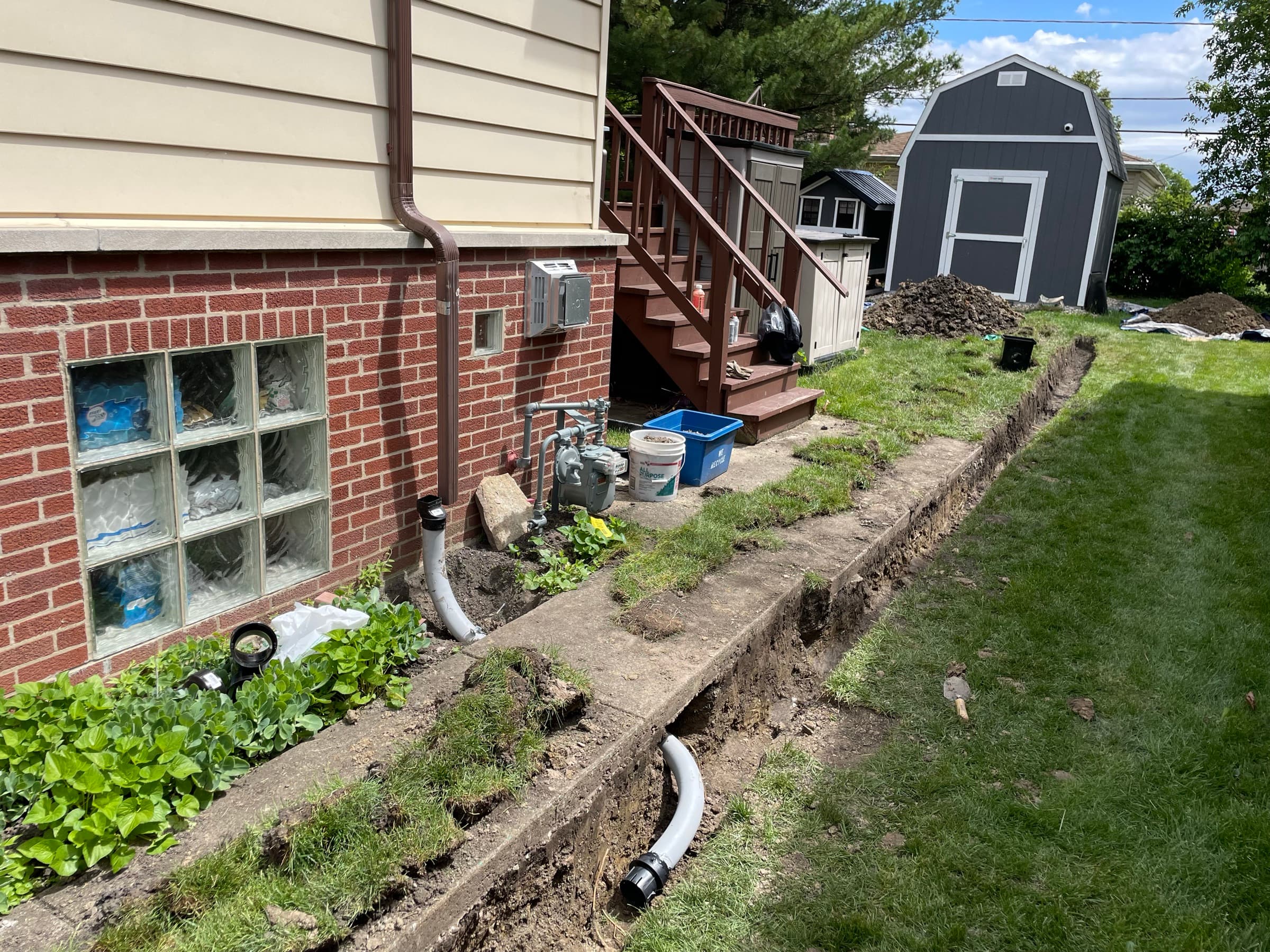 Open trench along a house foundation with white drain pipe laid in and bedded