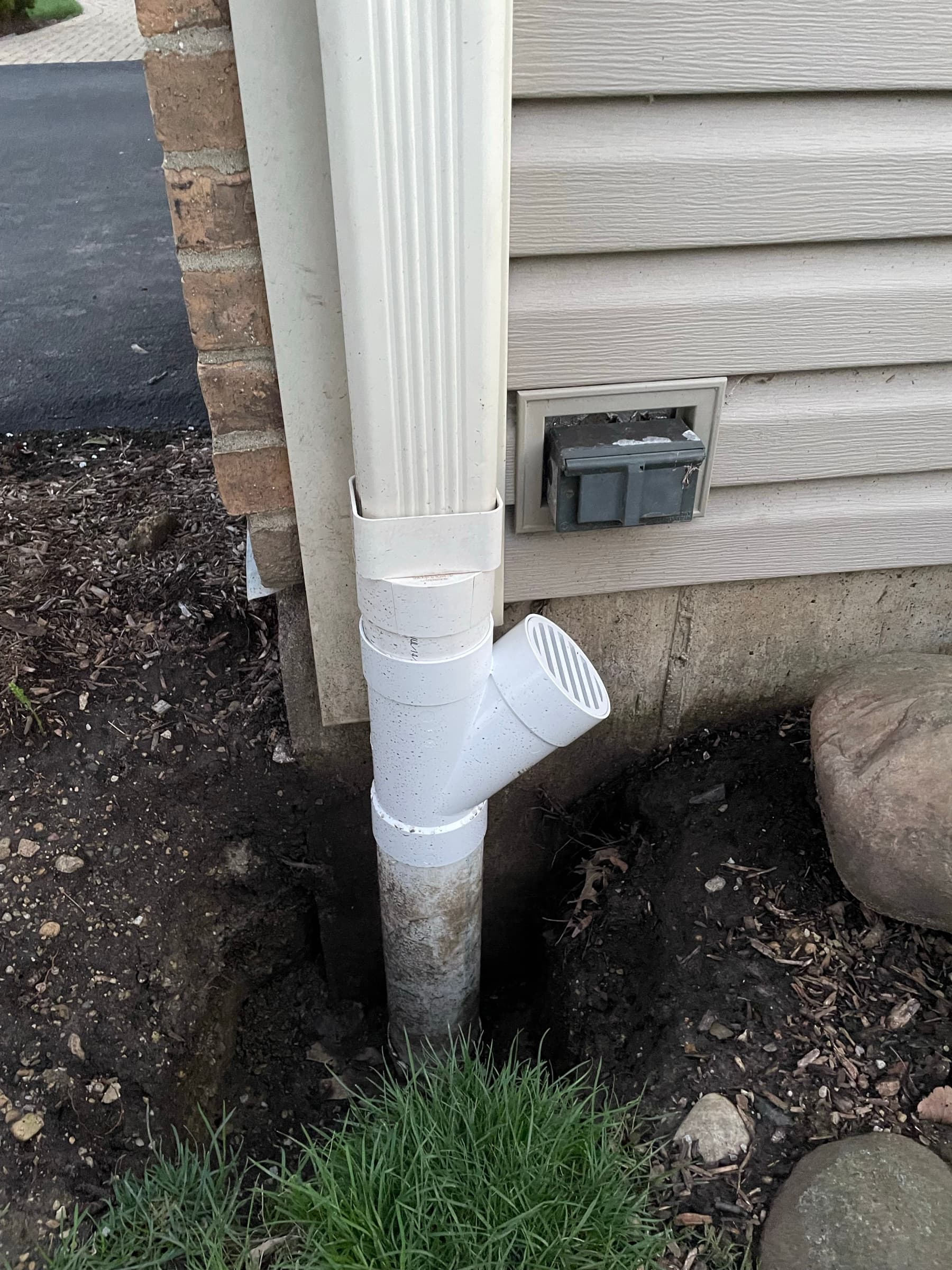 Downspout tied into a buried drain line with a fitted wye at the foundation