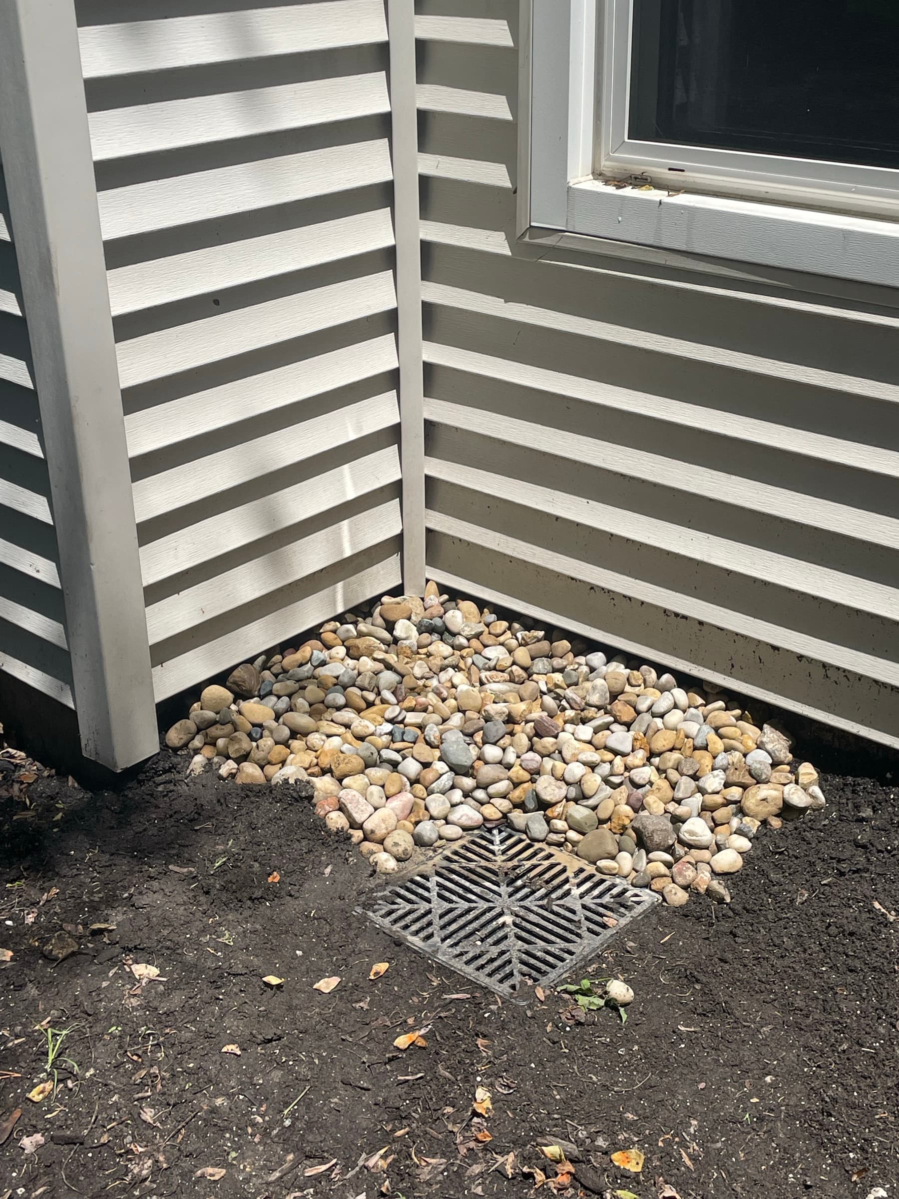 Drain grate set into a river-rock splash bed at the corner of a house