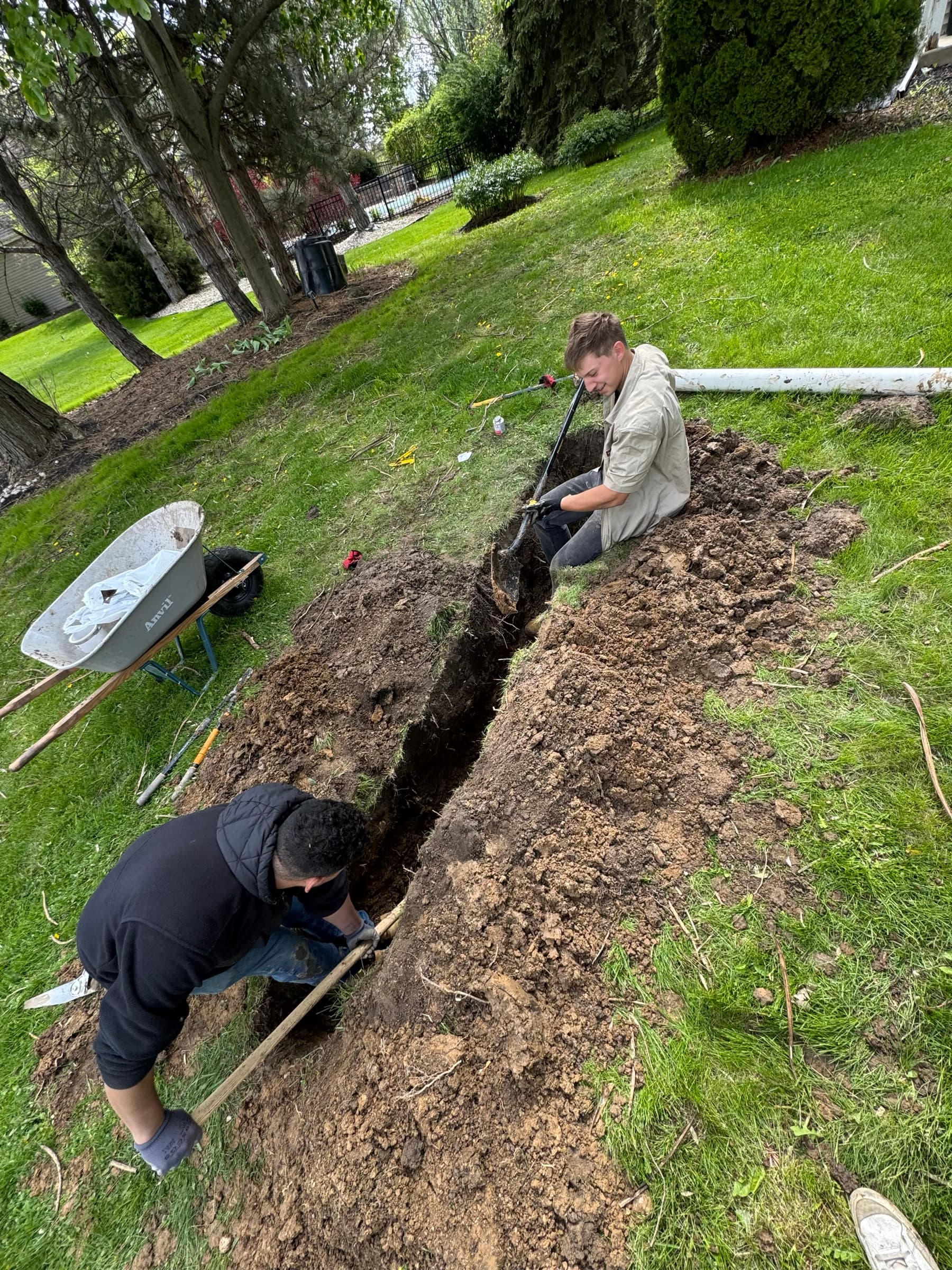 Two FCL crew hand-digging a narrow trench across a front lawn