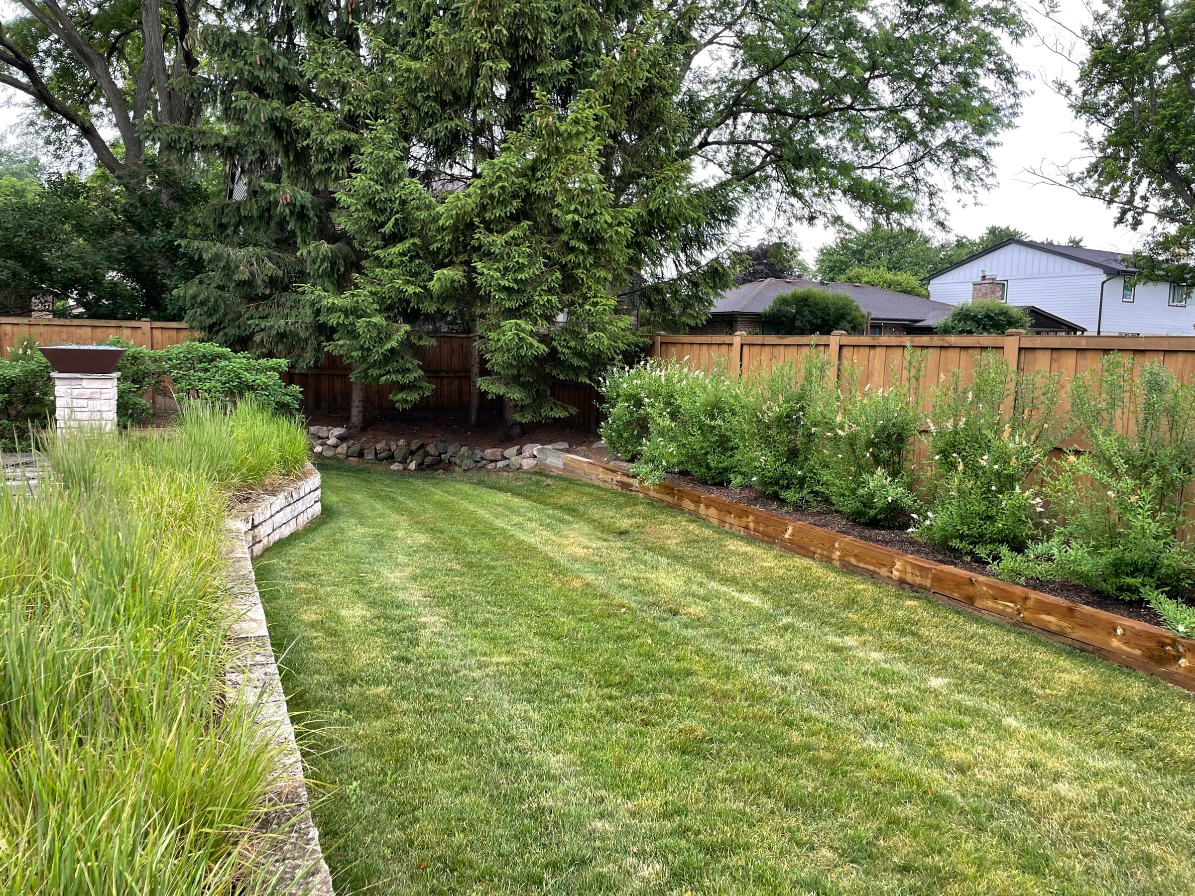 Rebuilt back garden: striped lawn, a timber-edged shrub bed along the fence and ornamental grasses by a block wall