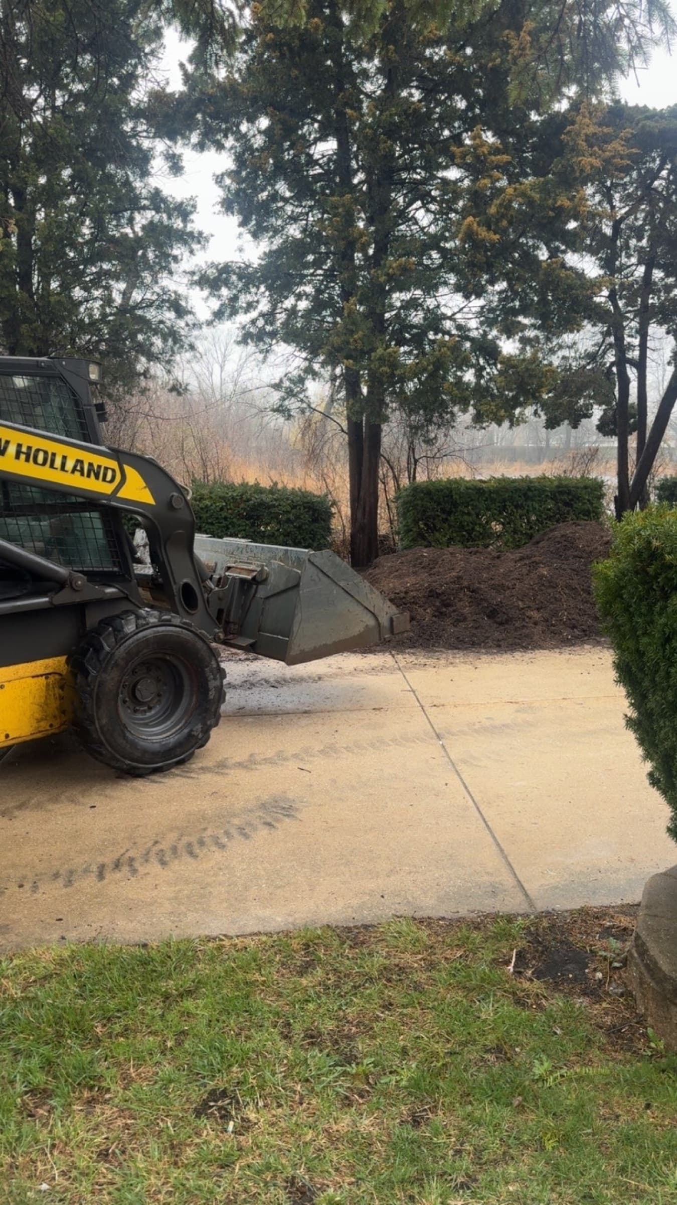 Skid steer on a driveway beside a long run of fresh mulch ready for the beds