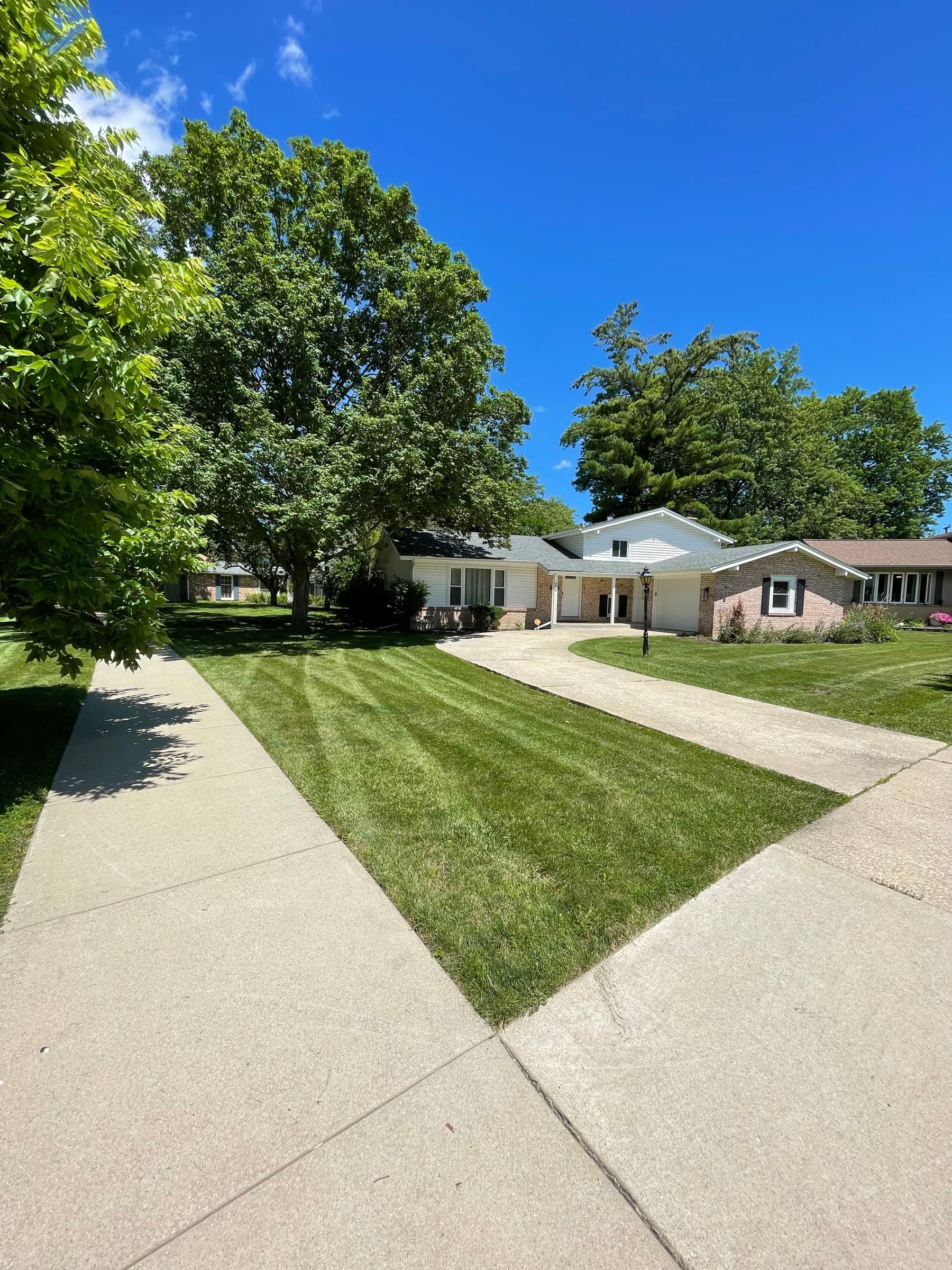 Freshly mown front lawn with clean mower stripes running toward a ranch house under a deep blue sky