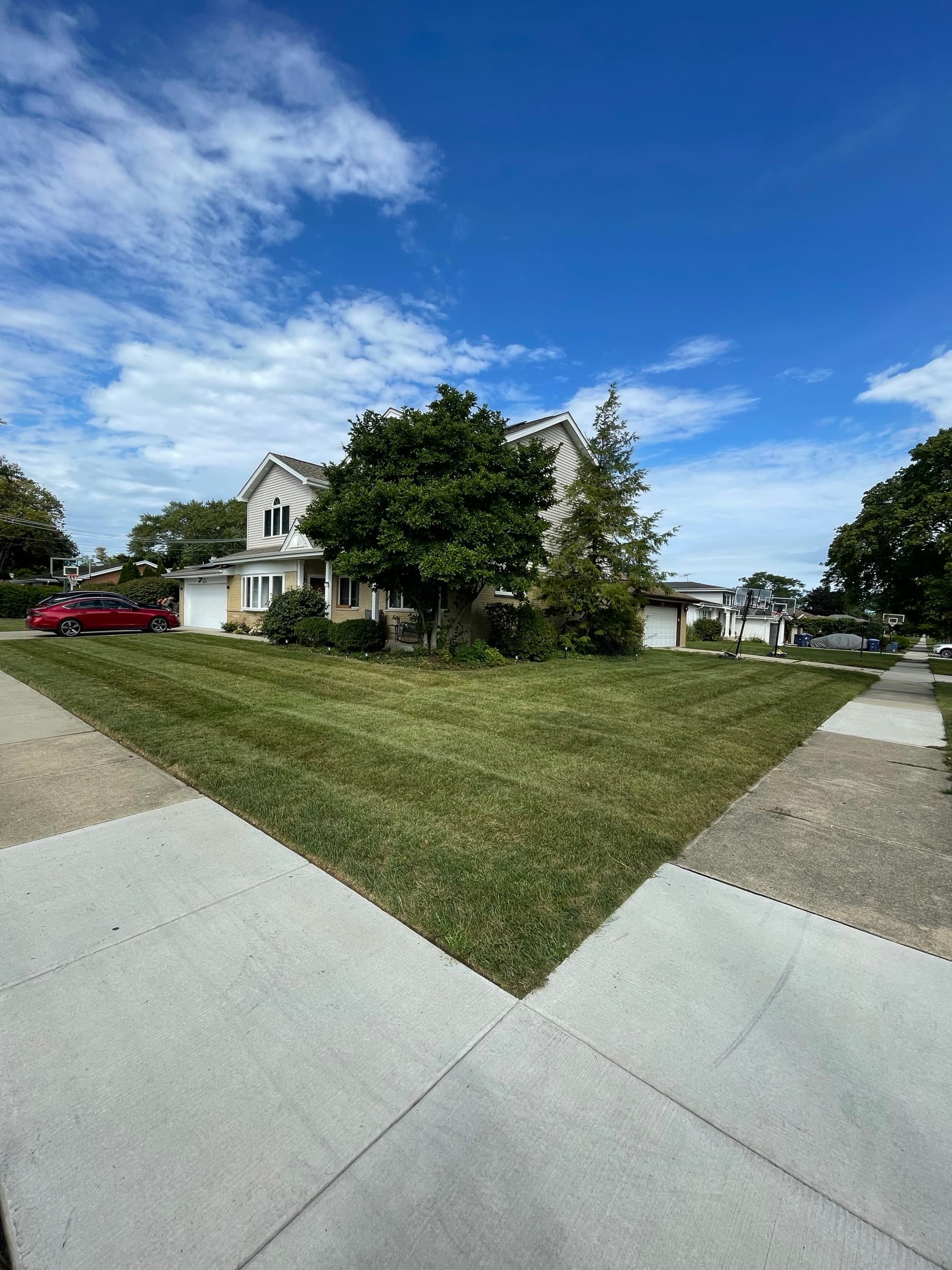 Corner lot mown in alternating stripes beside a two-storey house