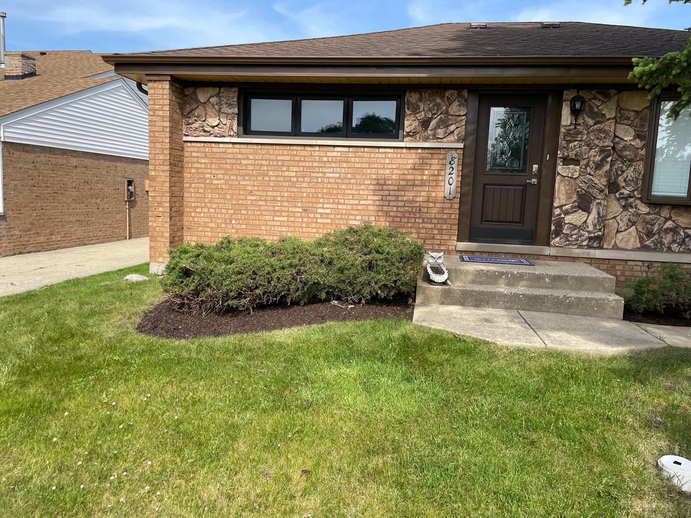 Brick ranch with clipped junipers in fresh dark mulch and a neatly cut lawn