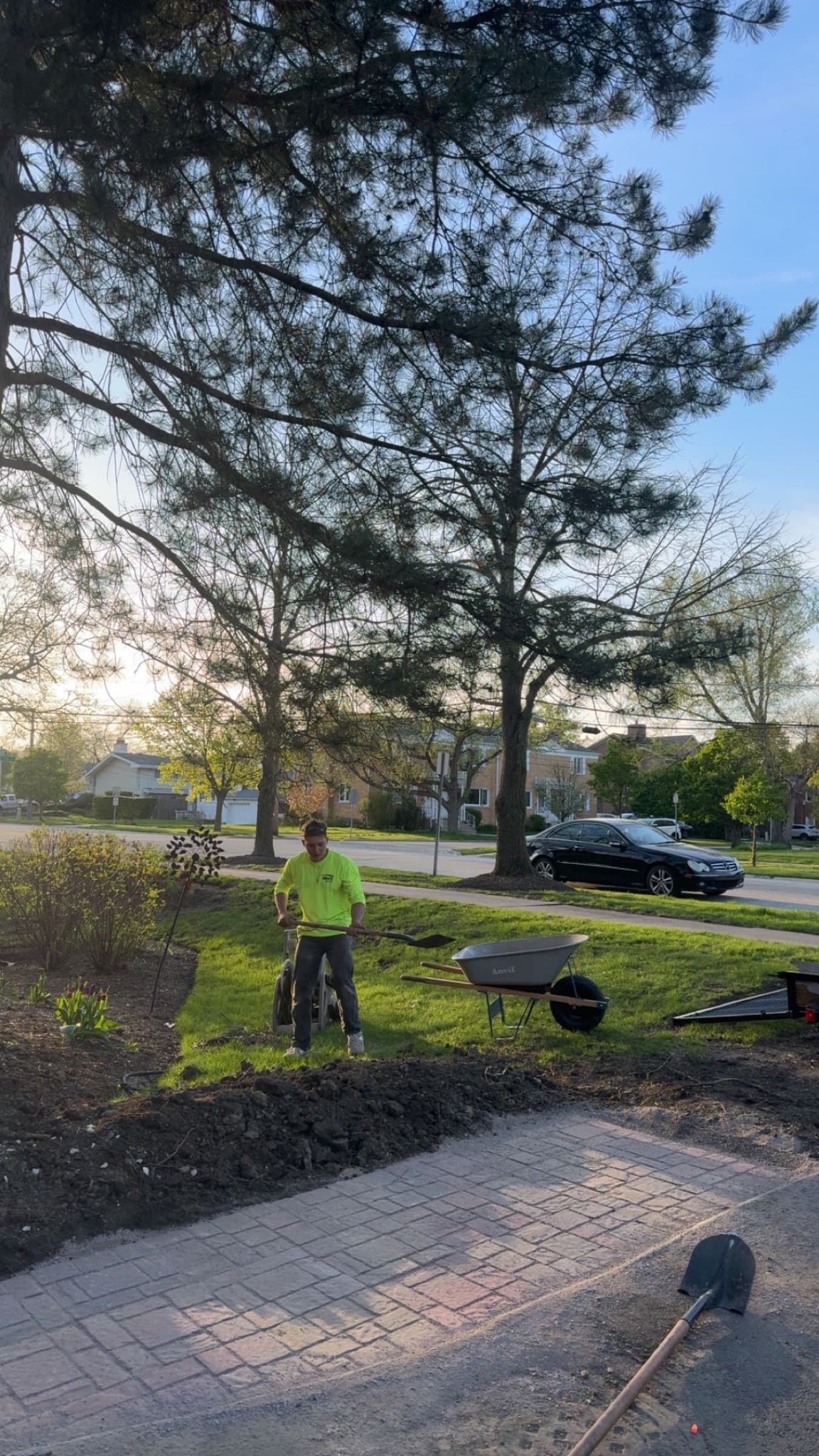FCL crew member raking a lawn at first light beside a paver driveway