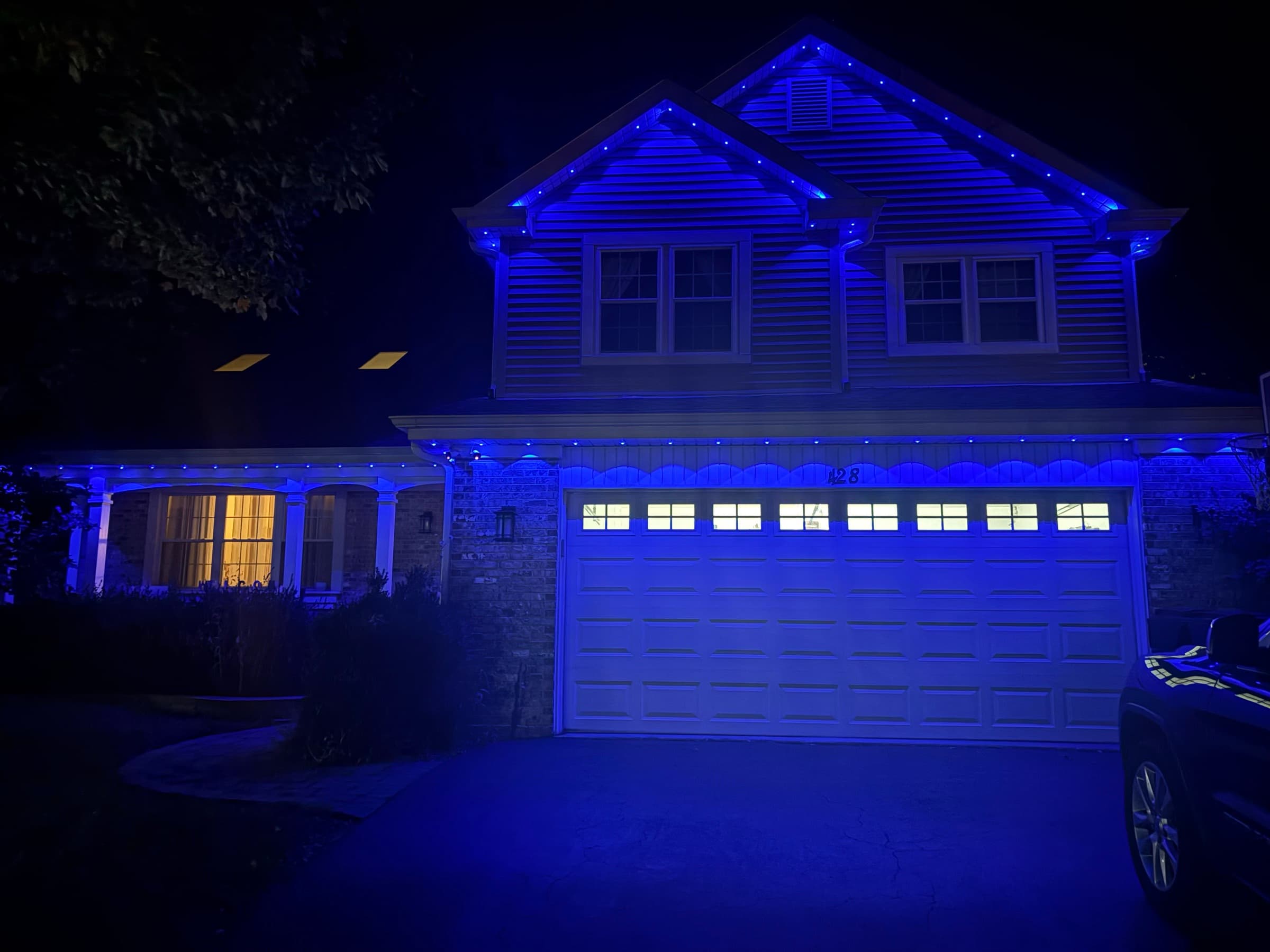 Permanent roofline lighting set to deep blue across the eaves and gables of a two-storey house at night