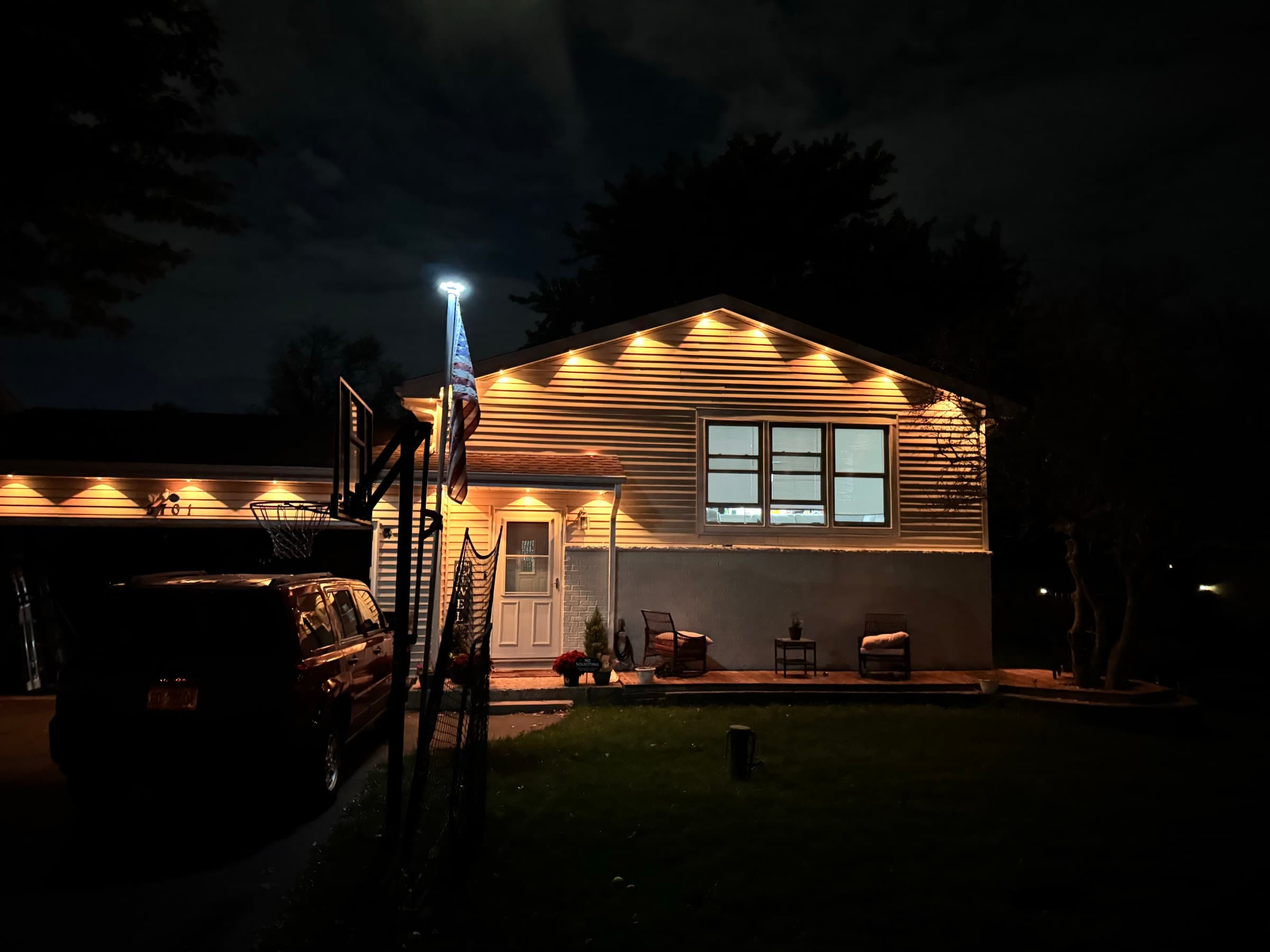 A whole house front lit in warm white by permanent roofline fixtures, tracing the gable and the garage eave after dark