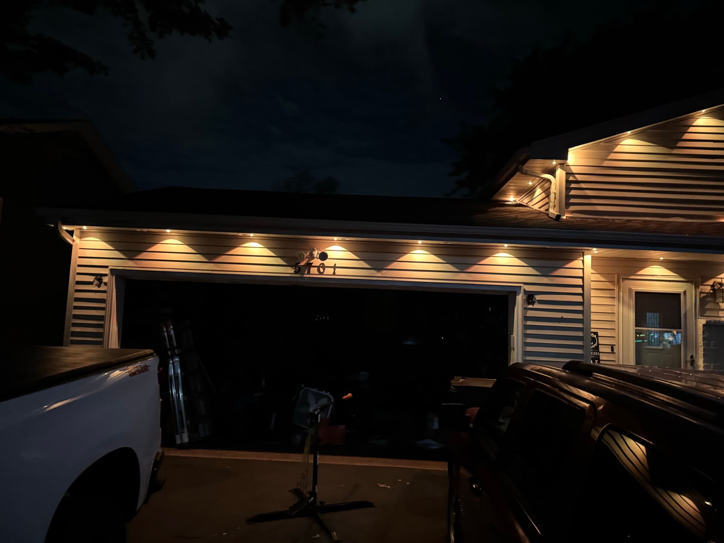 Evenly spaced permanent fixtures washing warm white light down the siding above a garage door at night