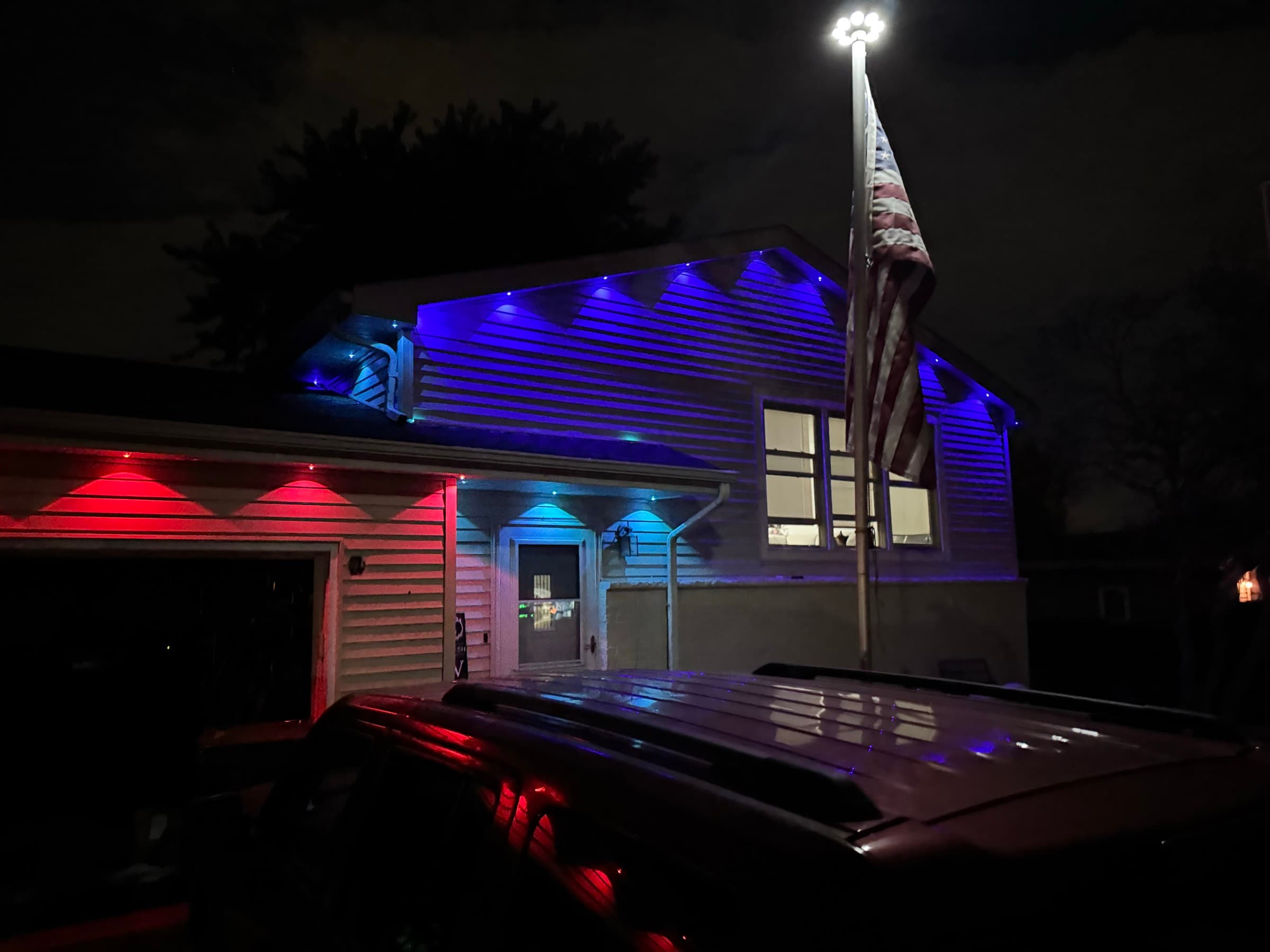 Permanent roofline lighting set to red and blue beside a flagpole for a national holiday