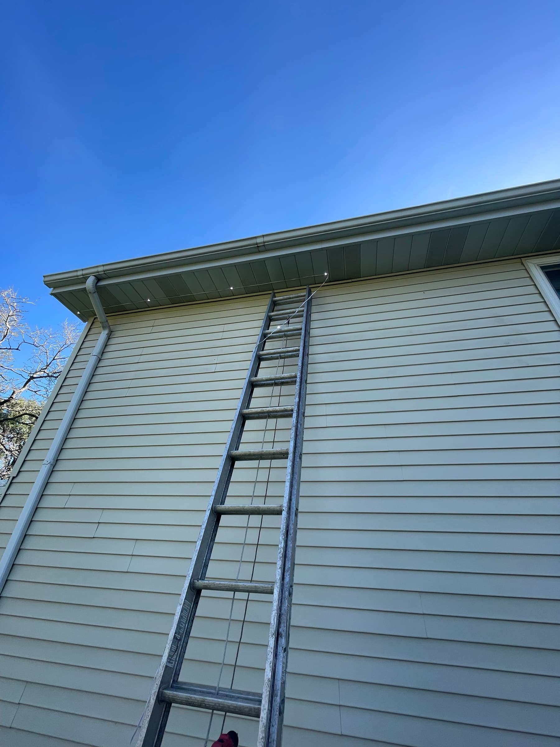 Daylight view of the track being run under a soffit during installation, showing how the fixtures mount permanently rather than hanging as a seasonal strand