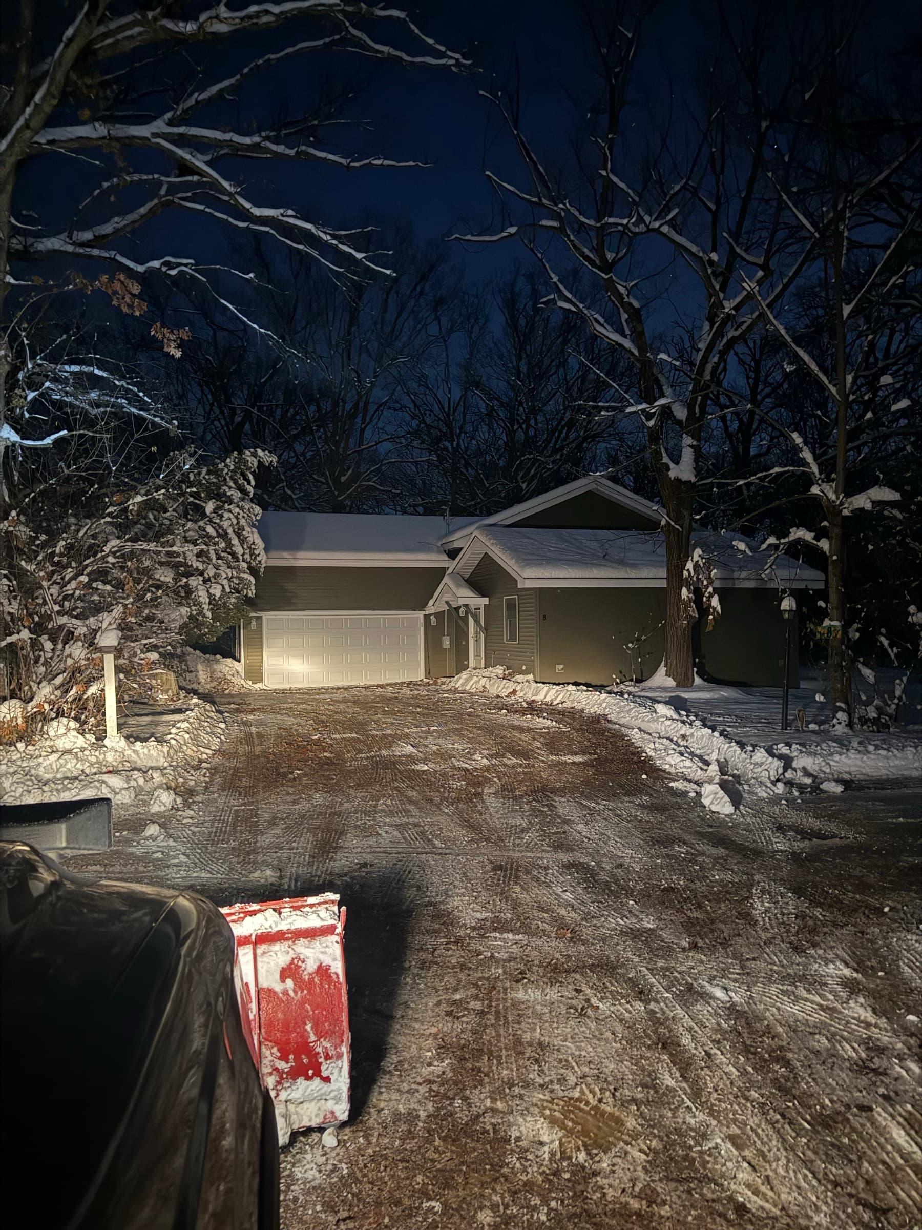 Plow blade clearing a residential driveway at night under house lights